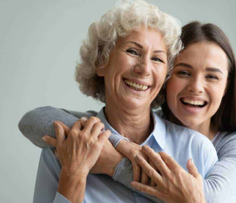 A woman and an older woman hugging each other in a home care setting.