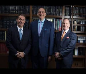 Three P.C. attorneys in suits standing in front of a Gersowitz Libo & Korek bookcase.